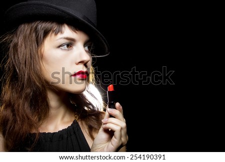 stylish caucasian female putting on red lipstick on black background