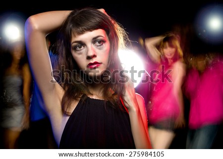 Disheveled drunk or female high on drugs at a nightclub.  Motion blurred party people in the background dancing.
