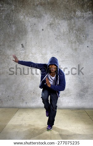 Active young black male dancing hip hop style in an urban setting.  He is wearing a blue hoodie and is on a concrete background with copyspace.