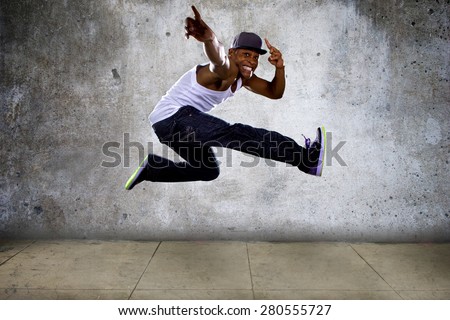 Black urban hip hop dancer jumping high on a concrete background.  The man is doing parkour or leaping.