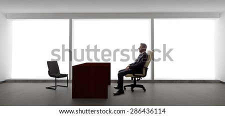Businessman with an empty chair waiting for a late client.  He looks upset and stressed.  The lonely mood is set by the back light from the large windows.
