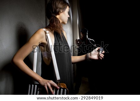 woman using a pepper spray for self defense against mugger in a dark alley.  She is using a canister of mace for security against a criminal.  The robber is hiding in the dark shadows.