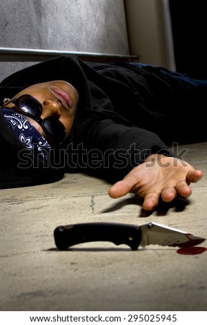 man in a street alley killed with a knife with blood and murder weapon. the man is laying dead or dying.  this version contains blood.