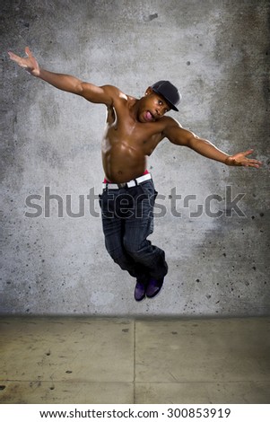 Healthy muscular black man jumping to show agility and energy.  The excited urban break dancer is on a grunge concrete background.