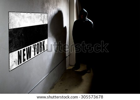 Hooded hip hop rapper next to wall graffiti with copy space.  The man is standing in a dark alley and a spray painted concrete wall.