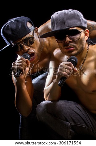 Rap concert with two muscular shirtless men with microphones.  The musicians are hip hop artists.