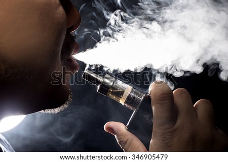 Man with concealed identity smoking a controversial vape.  Vaping is debatable in the health community if it is safe or a health risk.