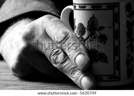 An old mans hand about to pick up a mug of tea, black and white background