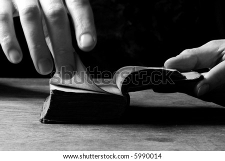 Woman turns the page in an old little bible or book, black and white background