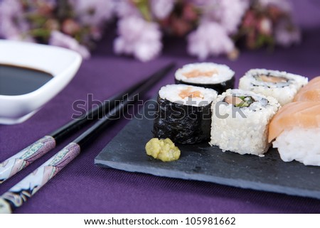 Various kinds of sushi on stone plate with chopsticks and a cup soy sauce besides