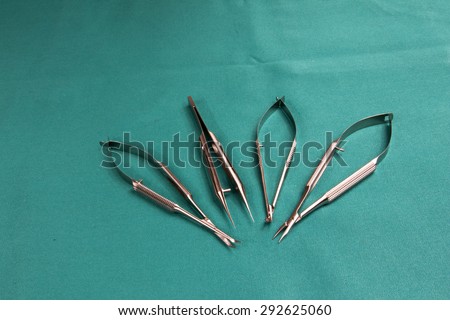 Four tools for eye microsurgery procedures.Scissors soft curve,Forcaps with platform,Micro-needle holder curved,Micro - corneal scissors curved.Tools on a blue tablecloth operating.Horizontal view.