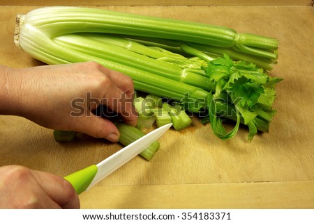 Housewife with a knife cuts fresh celery on an old wooden pastry board. Close,horizontal view.