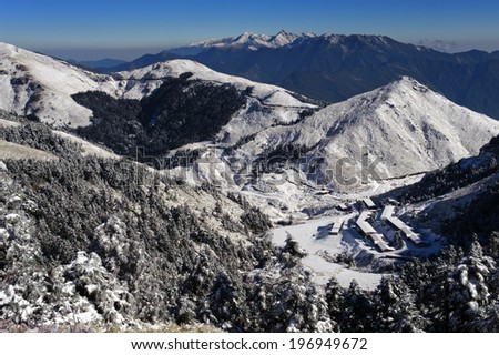 An aerial view of snow capped mountains and trees with buildings in the valley.