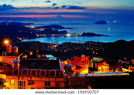 A darkened blue and pink sky over the ocean next to a brightly lit town.