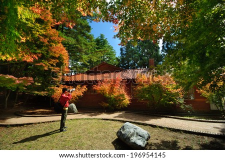 A person with a camera looking at a building surrounded by trees.