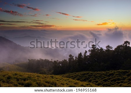 Sun shining in the horizon over clouds and tree covered hills.
