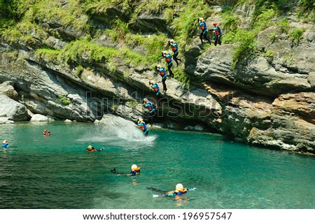 A pool of water at the base of mossy cliffs and people jumping in.