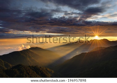 The sun shining between the clouds and the mountains.