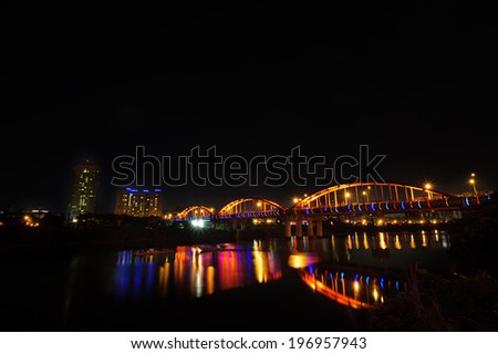 A bridge lit up at night with skyscrapers in the background.