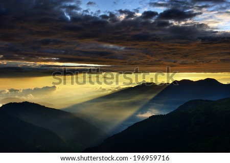 Sun rays coming through a cloudy sky towards hillsides below.