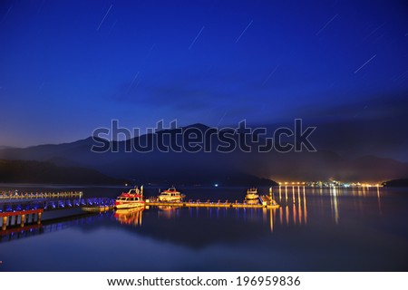 Boats in an illuminated harbor against a mountain scene at night.