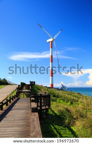 A wooden walkway and grass near a striped windmill.