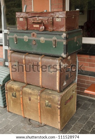 Old traditional leather luggage stacked high on railway platform.