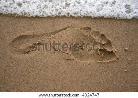 Foot print on a Sandy Beach with a wave washing over
