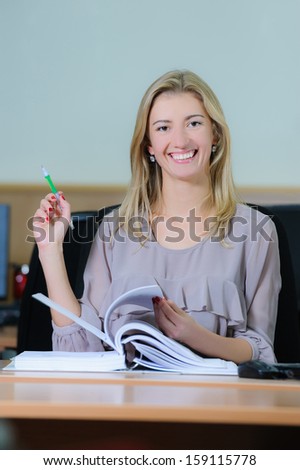 Smiling young girl in the office sitting at a table flipping a book with a pen