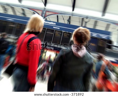 Zoom blur on busy train station of two women checking departure times