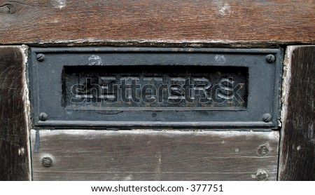Old metal letterbox or mailbox flap on old wooden door.