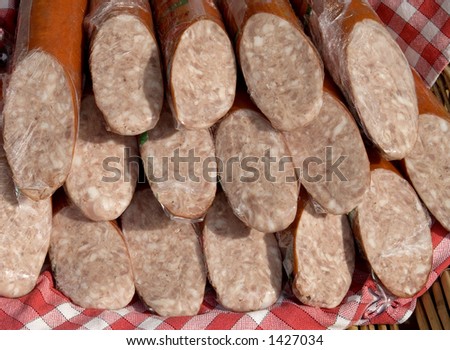 Display of French garlic and pork slicing sausage wrapped in plastic on red and white check cloth. Shallow depth of field.