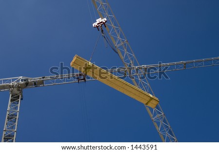 Low-angle view of tower crane lifting timber, second crane behind, against blue sky