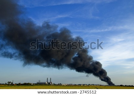 Huge plume of black smoke from fire rising high above flat land against blue sky