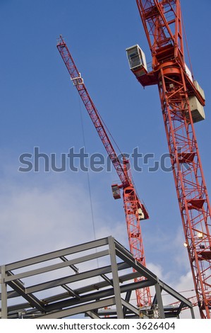 Two red tower cranes and gray structural steelwork against blue sky.