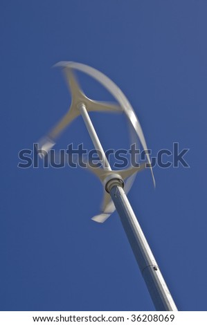 Low angle diagonal view of vertical axis wind turbine with motion blur on blades against a clear blue sky