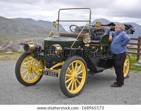Co. Kerry, Ireland - July 11 2006: A Senior Man, Proud Owner Of An Elegant Vintage Car From The Edwardian Era, Stands Beside His Vehicle In A Roadside Car Park In The Kerry Mountains.