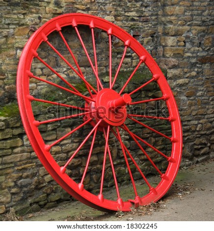 Vintage cast iron carriage or cart wheel painted red, leaning against an old natural stone wall
