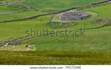 Ancient iron-age stone fort with interior enclosures, near Coomakista Pass on the Ring of Kerry, Ireland, set amid typical Irish scenery of green fields, stone walls and farm animals.