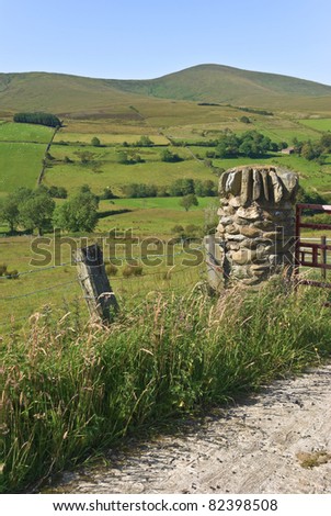 Hill farming in the Sperrin mountains, Co Londonderry, Northern Ireland. A pillar built from local rock makes a typical gate post and sheep graze in little stone walled fields on a sunny summer day.