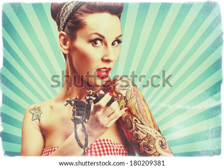Photo of beautiful pin-up girl with tattoos and tattoo machine tattooing herself and looking at the camera. Retro styled imagery, toned image, grungy, noise added.