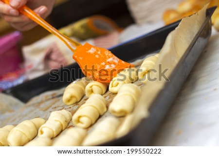 Baker putting whisked egg coat on top of freshly rolled up mini croissants just before baking them