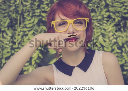 Cute hipster teenage girl with mustache hand drawn on  a finger she placed over her lips, cute and funny. Retro colors