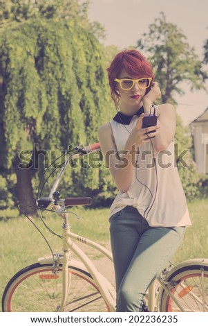 Hipster teenage girl on her vintage bike, listening to the music on her purple smart phone. Retro colors, toned image