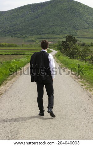 Businessman on the road, looking up to the mountain ahead. Walking with his back to the camera