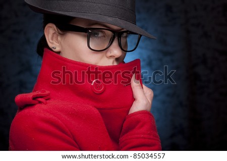 Portrait of a young woman in red trench coat, with glasses, and blue background.Hiding the face.