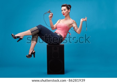 Photo of beautiful pin-up girl with tattoos and tattoo machine tattoing herself and looking at the camera