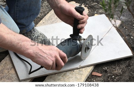 Craftsman is cutting a floor tile with a portable angle grinder