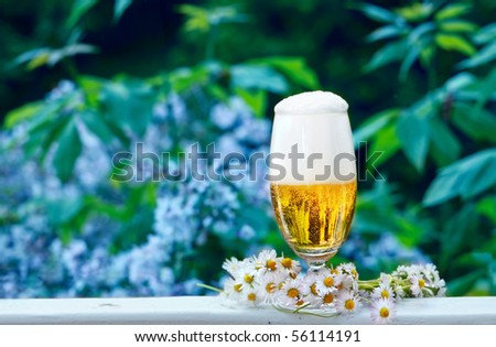 Glass of beer with garland of daisies, standing on the terrace in front of the garden