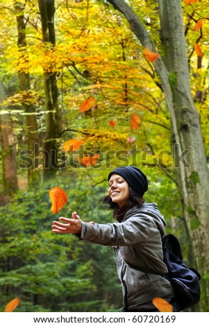 Beautiful smiling woman is catching falling leaves in the autumnal forest